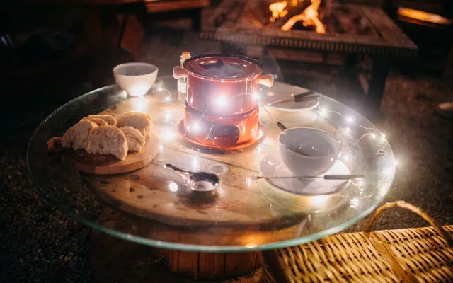 A fondue pot on a table lit by fairy lights in front of a fire