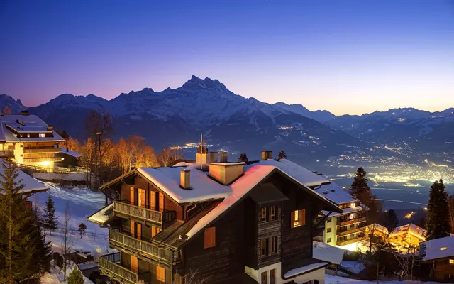 Chalets with lit windows and snowy roofs in Villars at dusk