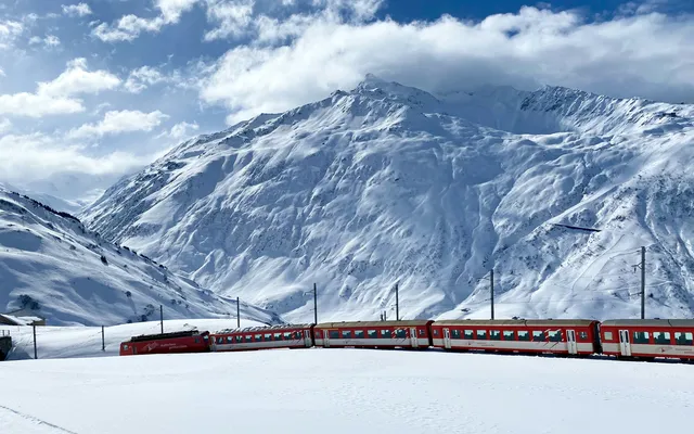The red Glacier Express below a sunlit snowy mountain near Andermatt